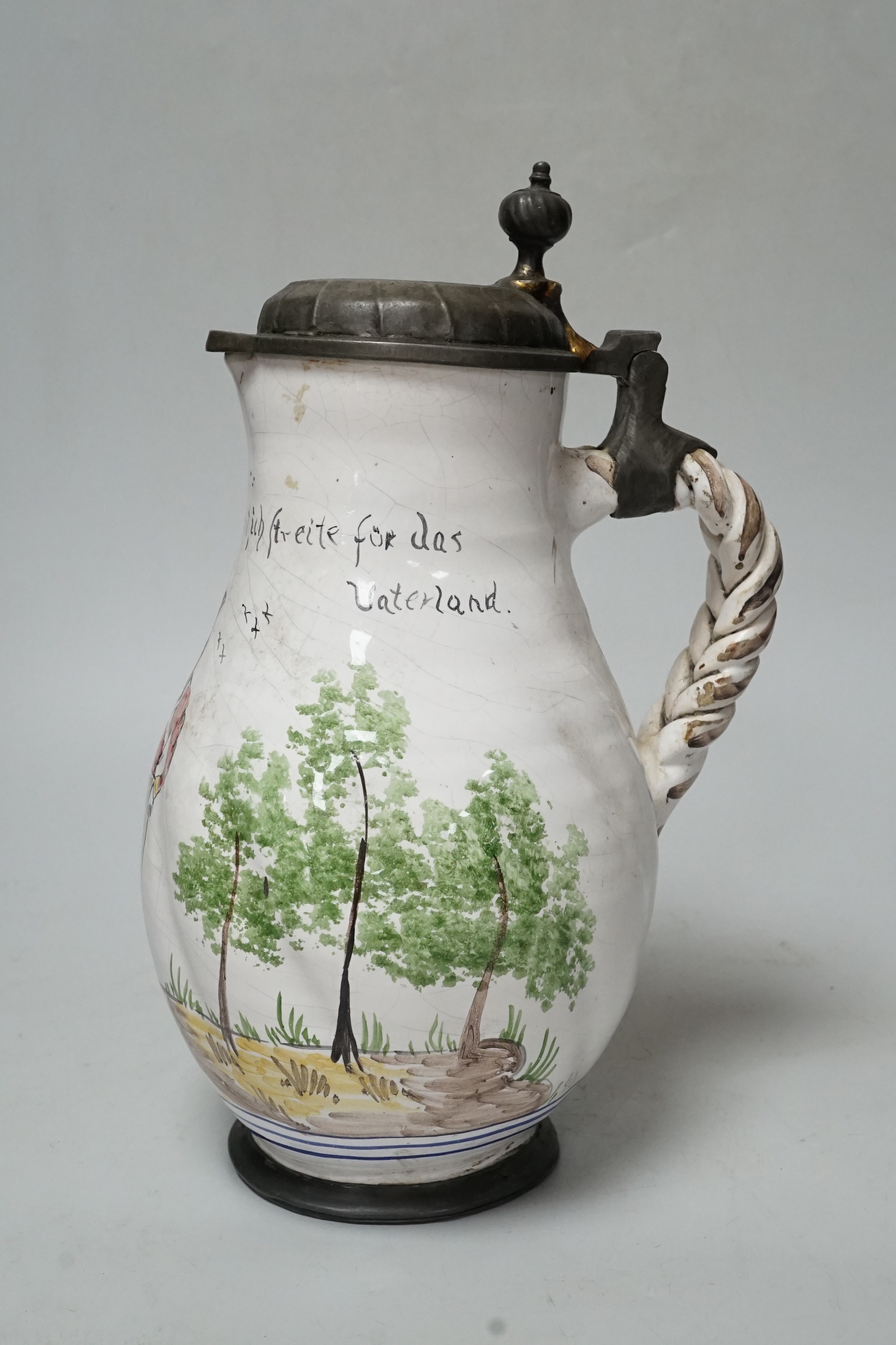 A large 18th century German faience pewter lidded jug, baluster shaped, with a naive painting of a soldier, inscribed ‘’Soldat, das ist bekqnnt, ich streite fur das vaterland’’ (Soldier, that is known for that fatherland